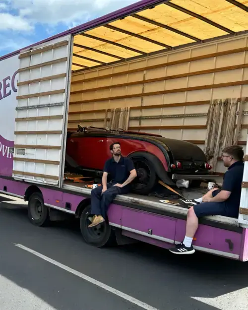 Regal Moving & Storage purple removal truck with side door open and a vehicle loaded, crew sitting on the side