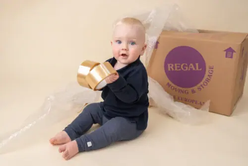 Baby sitting down holding packing tape with Regal Moving & Storage box and bubble wrap in the background