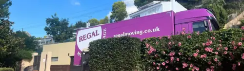 Regal Moving & Storage purple truck behind a hedge with flowers
