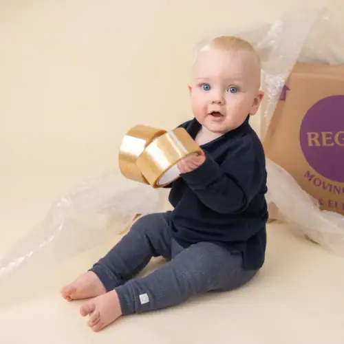 Baby sitting down holding packing tape with Regal Moving & Storage box and bubble wrap in the background