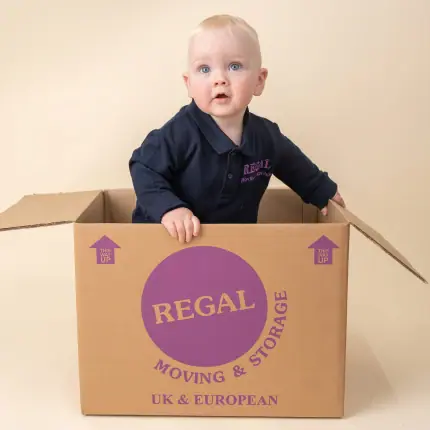 Baby standing inside a Regal Moving & Storage box with packing materials nearby