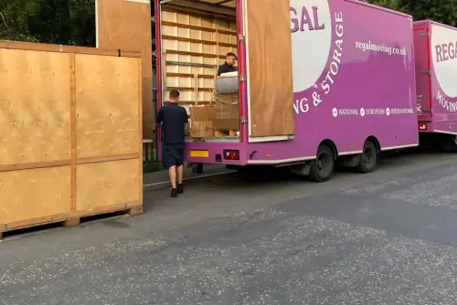 Regal Moving & Storage truck with trailer, door open, crew loading items from a container
