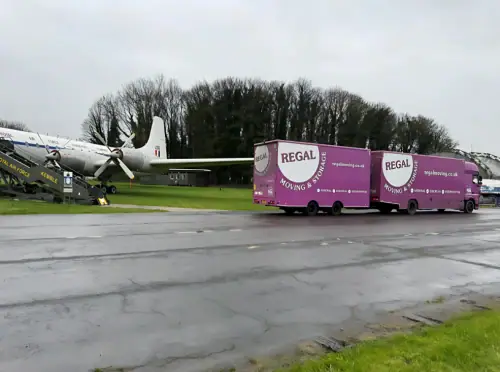 Regal Moving & Storage purple truck parked on an airport runway beside a plane