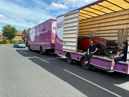 Regal Moving & Storage purple removal truck with side door open and a vehicle loaded, crew sitting on the side