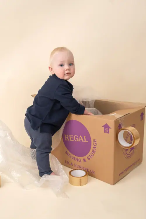 Baby standing beside Regal Moving & Storage box with bubble wrap and packing tape